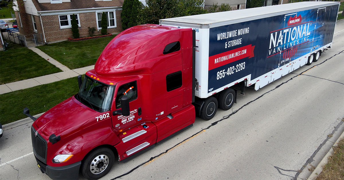 A National Van Lines truck sits parked in the street in a residential neighborhood. The National Van Lines BBB profile states that they have an A+ rating, the highest a company can achieve. 