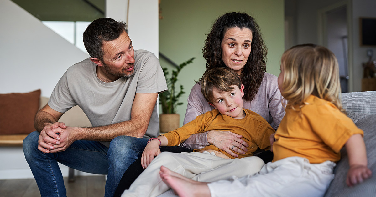 Two parents talk to their two children in their home. They are planning a long distance move, and are having a family discussion on what will happen during the process.