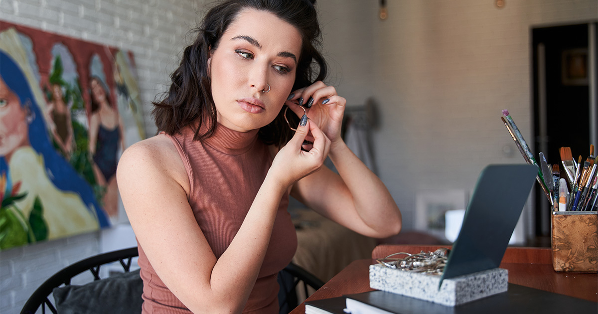 A woman looks through her jewelry box at her desk, while trying on a pair of hoop earrings. 