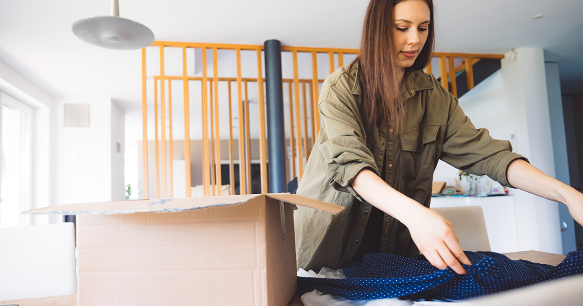 A woman sorts and packs her clothes into moving boxes. She is diagnosed with ADHD, and is using different tactics to manage moving with ADHD comfortably. 