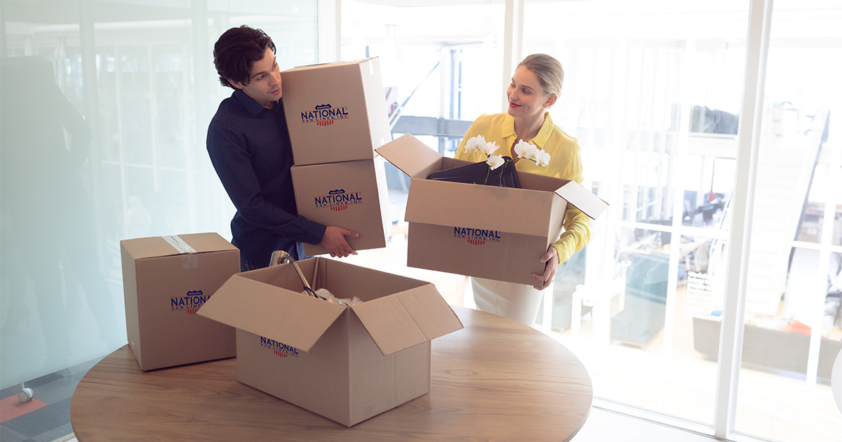 Two coworkers put down National Van Lines moving boxes on a table in in their new office. They have just completed a commercial move with their organization.