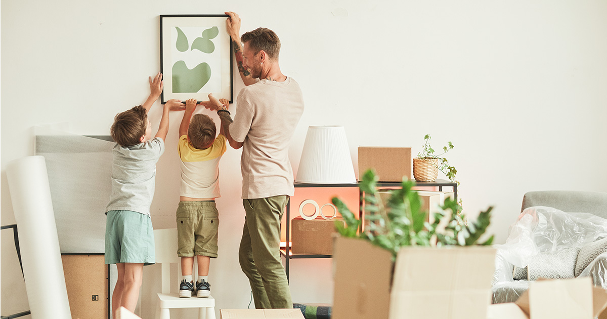A father and his two children hang up a picture in their new home after a long distance move. 