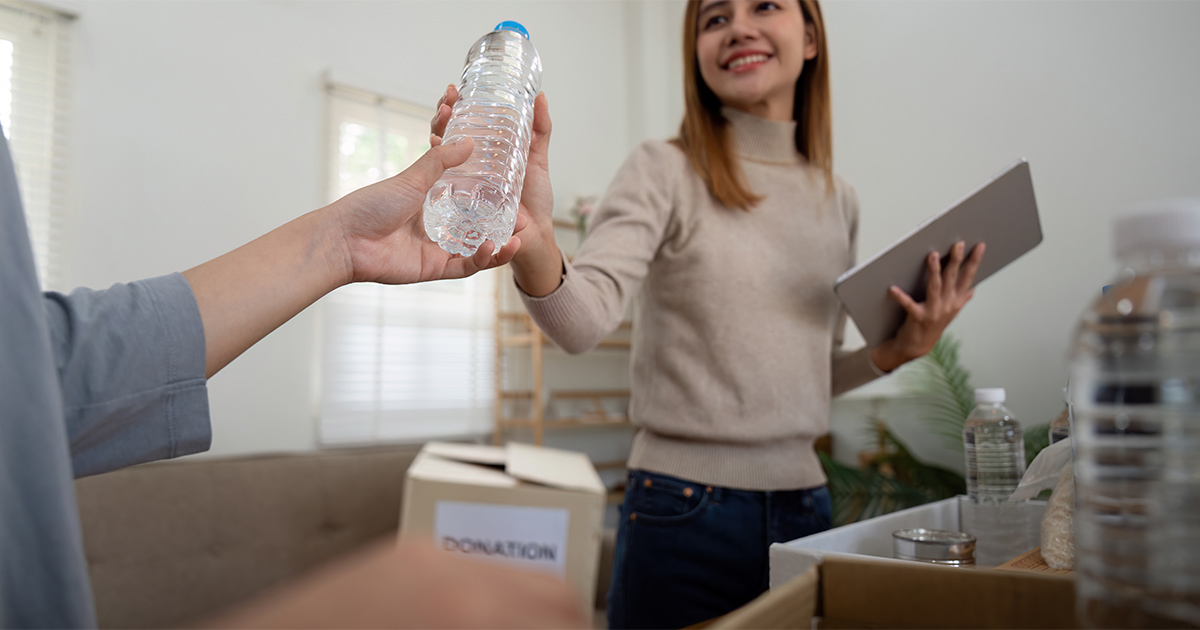 A woman hands someone in her moving crew a bottle of water. She holds a table with a moving checklist on it. She is showing her appreciation to the crew for their part in her long distance move.