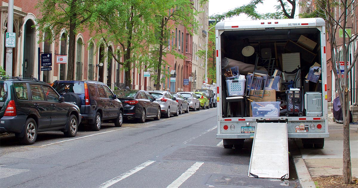 An open truck filled with boxes and items parked on a narrow city street. 