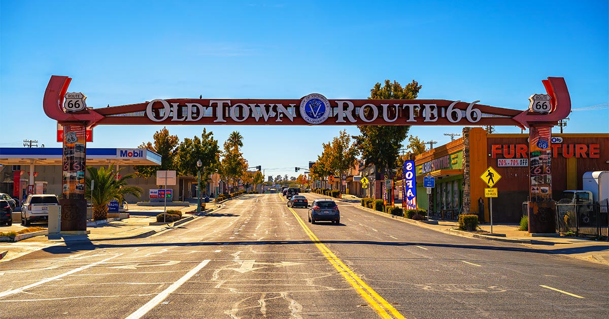 Vibrant street scene under the 'Old Town Route 66' neon archway sign in Victorville, CA featuring a clear blue sky and classic roadside attractions.