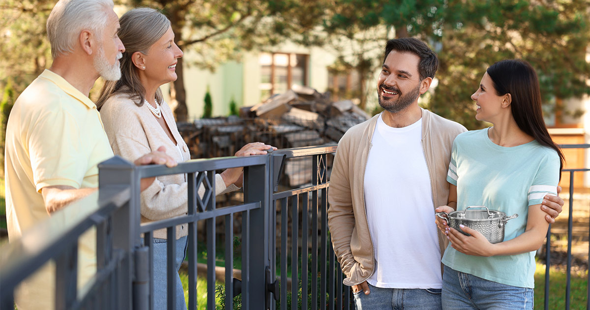 A young couple meets and greets their new neighbors over a fence after completing their long distance move to a new state.