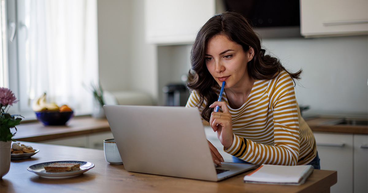 A woman, in her kitchen, reviews information about her upcoming long distance move on her laptop computer. 