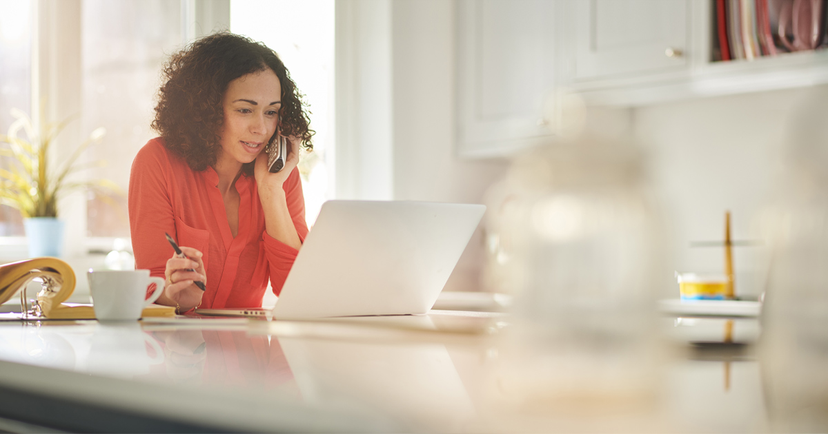Woman using a laptop computer while making a phone call to a moving company customer service department.