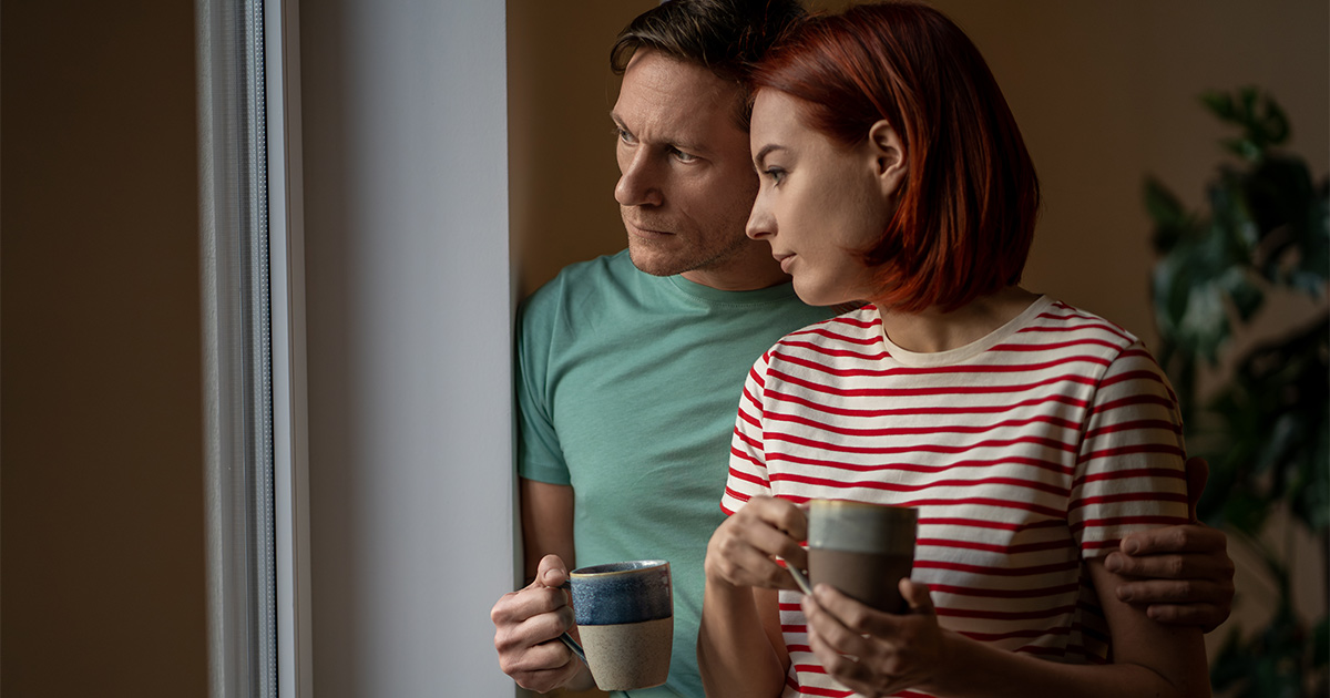 A concerned couple looks out a window.