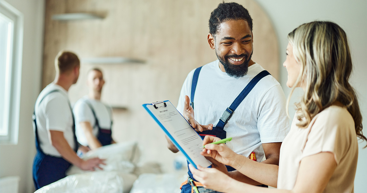 A woman holding a clipboard talking to a third-party moving professional. They are smiling. 