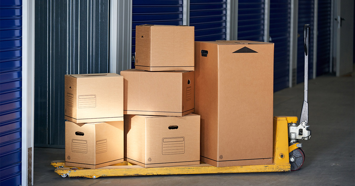 A stack of moving boxes in varying sizes, atop a yellow pallet in a storage unit. 
