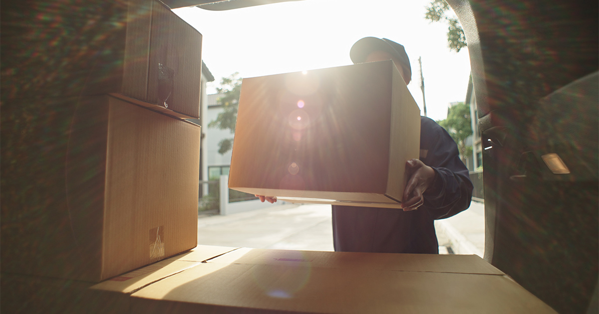 Someone loads a box into the back of a moving truck. 
