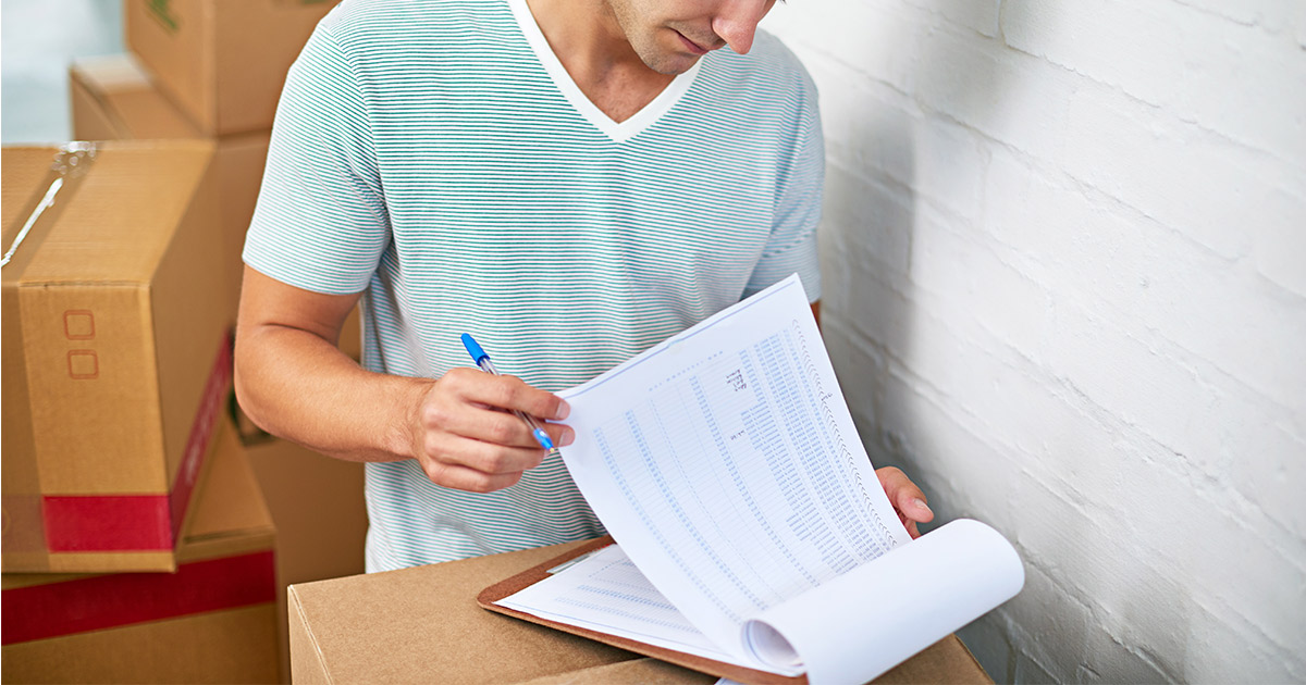 A man reviews a print-out copy of his long distance moving quote. He stands amongst moving boxes. 