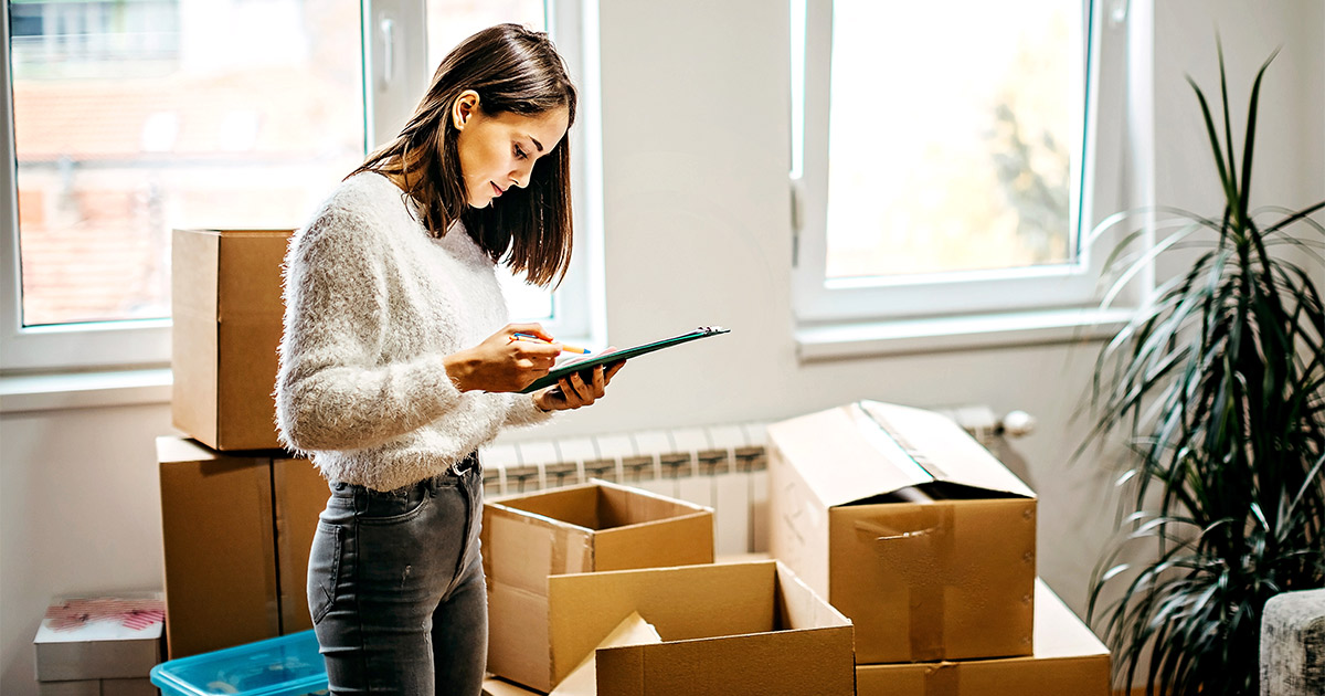 A woman reviews a checklist of the benefits she will receive from her full service movers. She is surrounded by moving boxes. 