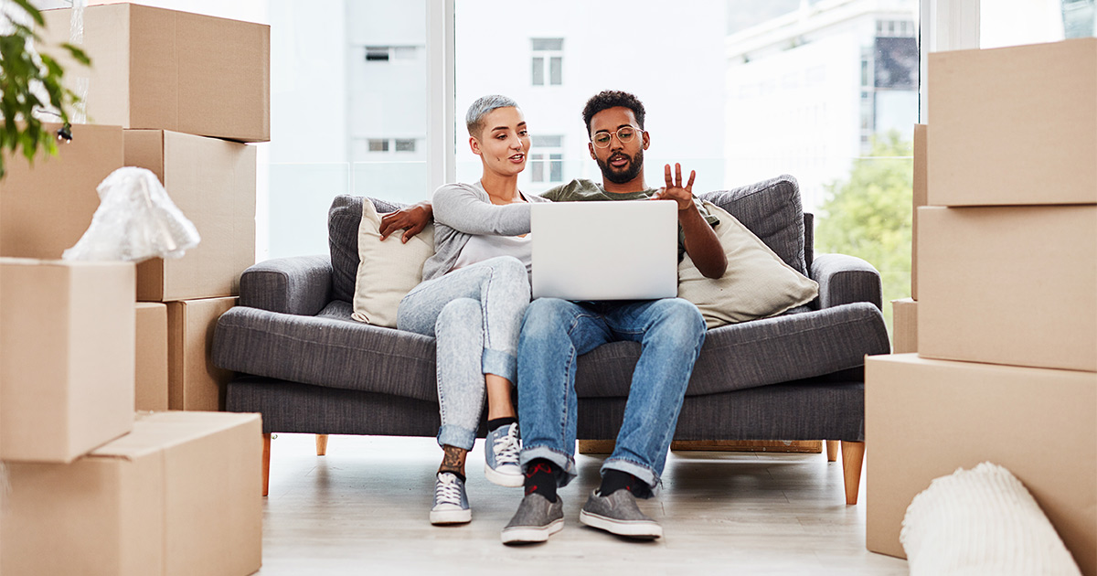 A couple sits on their couch amongst moving boxes and discuss the cost of moving. 