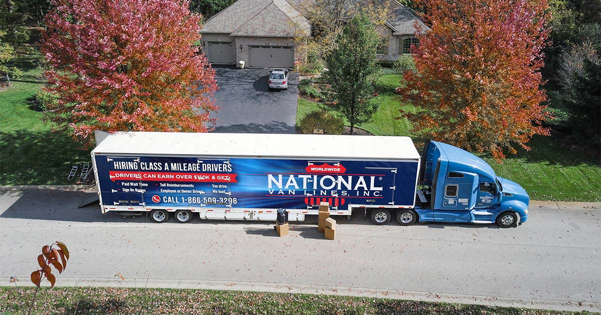 A National Van Lines moving truck is parked outside a suburban home. There are several moving boxes next to it.