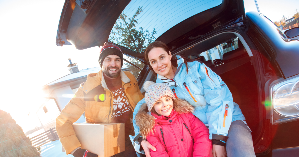 Parents and their child sit against their car with a taped moving box. They are moving during the holidays.