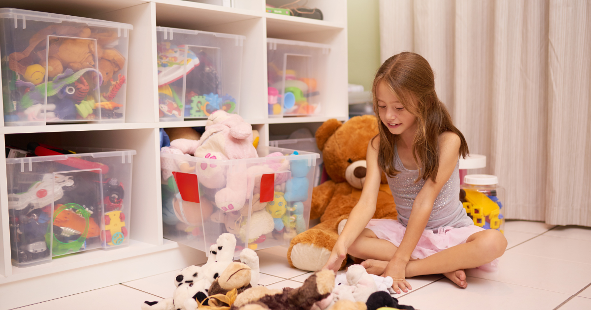 A young girl happily sorts through her toys and stuffed animals in her playroom. She is getting ready for a long distance move and is figuring out which toys to put into storage. 