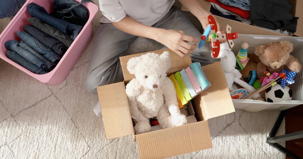 Someone packs various toys and stuffed animals into moving boxes before a long distance move. 