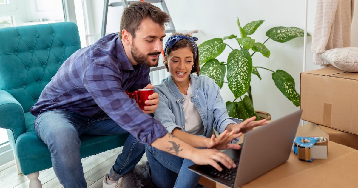 A man and woman sit amongst moving boxes and packing supplies. They are research BBB accredited moving companies for an upcoming long distance move. 