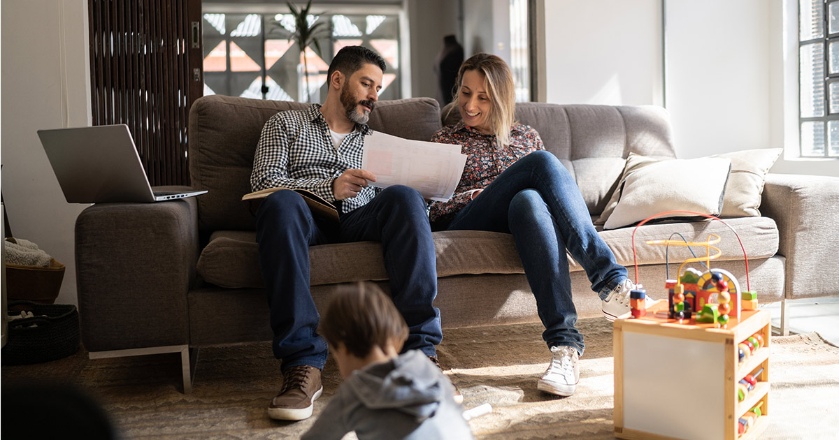 A couple sits on a couch and begins to plan their long distance move. Their child plays in the foreground. They are looking at the timeline for their upcoming move and wondering how far in advance they should book a mover.