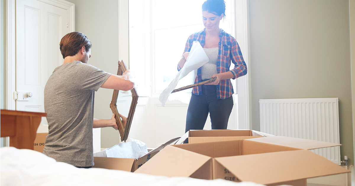 A couple unpacks mirrors from moving boxes after a long distance move. They are feeling hopeful because they overcame moving stress. 