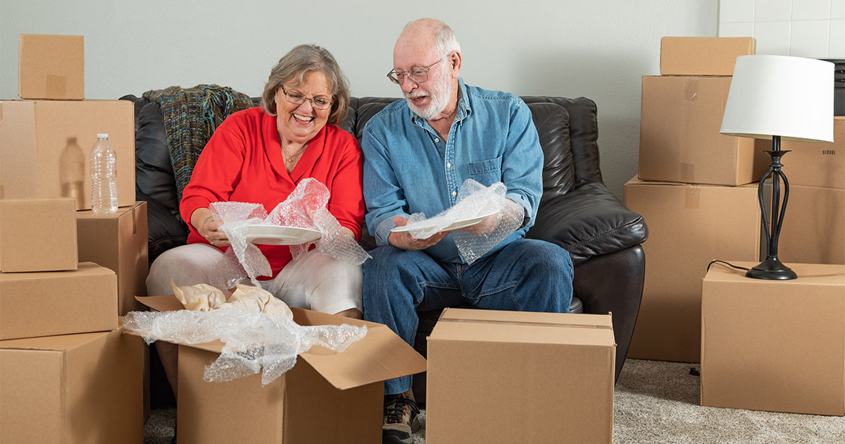 A senior couple wraps up their items into moving boxes. They have hired senior movers to help them with a long distance move. 