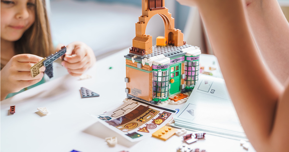 Two children sit at a table and assemble a Harry Potter Lego set. They have just moved long distance and are putting their Lego sets back together.