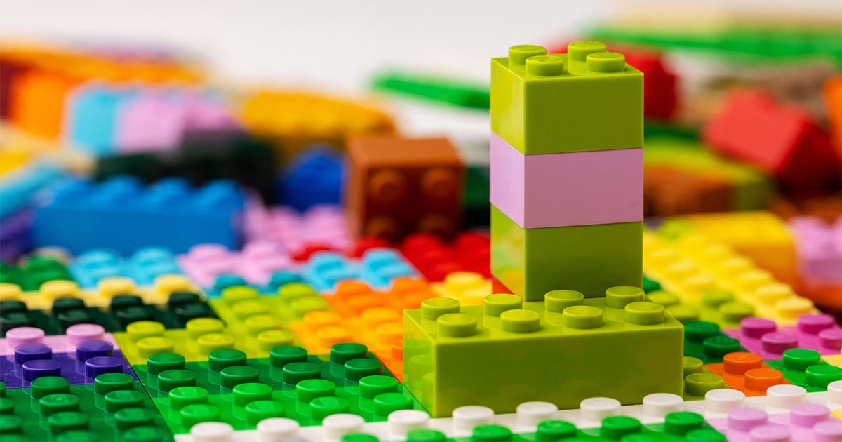 Lego bricks are shown stacked and strewn around. They are part of a collection that will be involved in a long distance move. The owner will need to pack the Legos for moving.