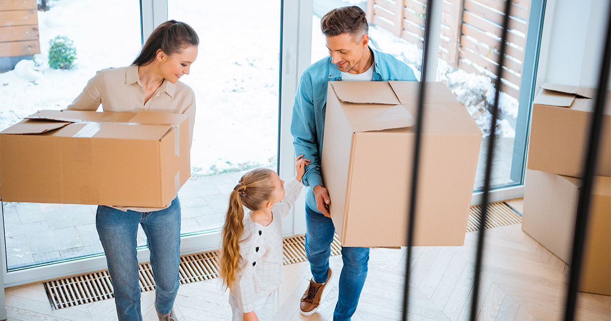 Two parents and their child carry moving boxes into their new home. They have just completed a winter move.