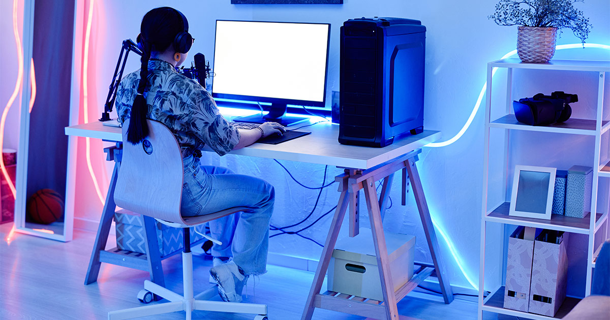 A girl with a braid sits in front of her gaming PC and streaming setup at a computer desk. Because she knows how to pack electronics for moving, she was able to reassemble her gaming setup with no issues at her new home.