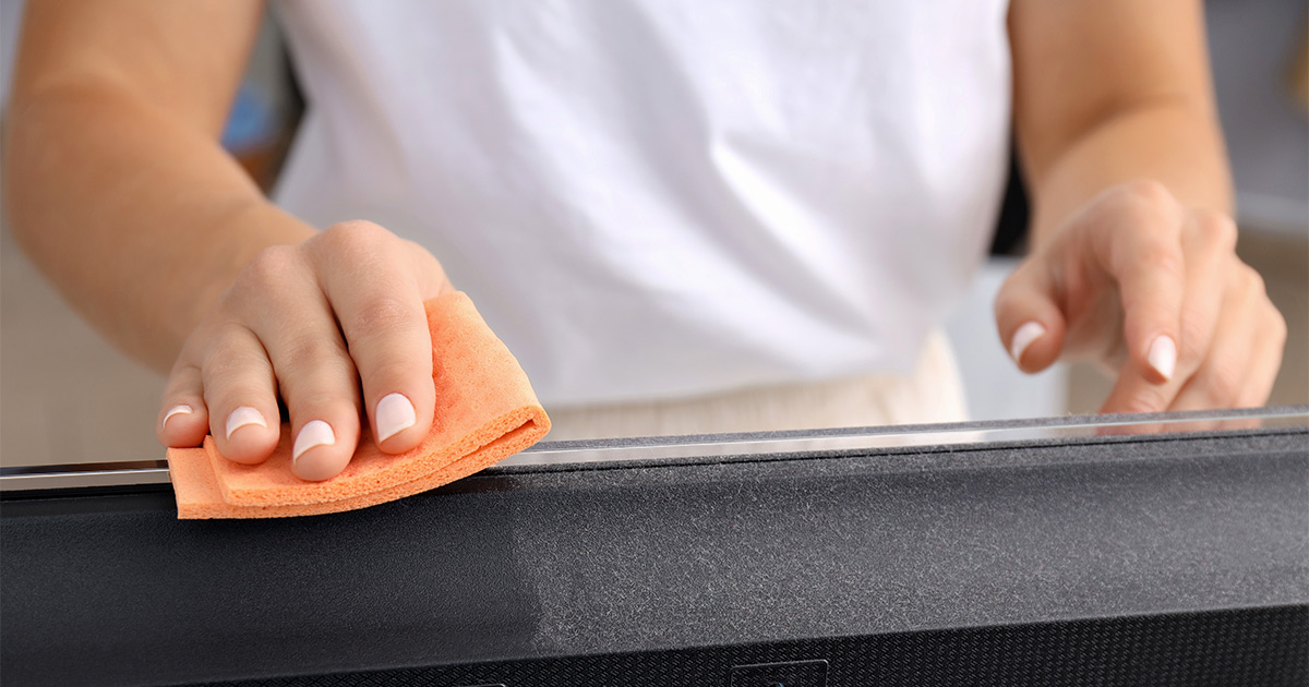 Someone uses an orange cleaning cloth to wipe off the top of a large PC monitor. They are cleaning because they know how to pack electronics for moving.