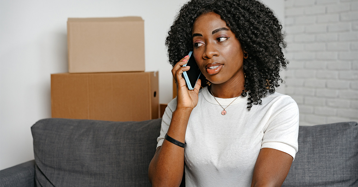 A young woman is on her phone speaking with an emergency moving company. She needs to move last minute and is getting moving quotes.
