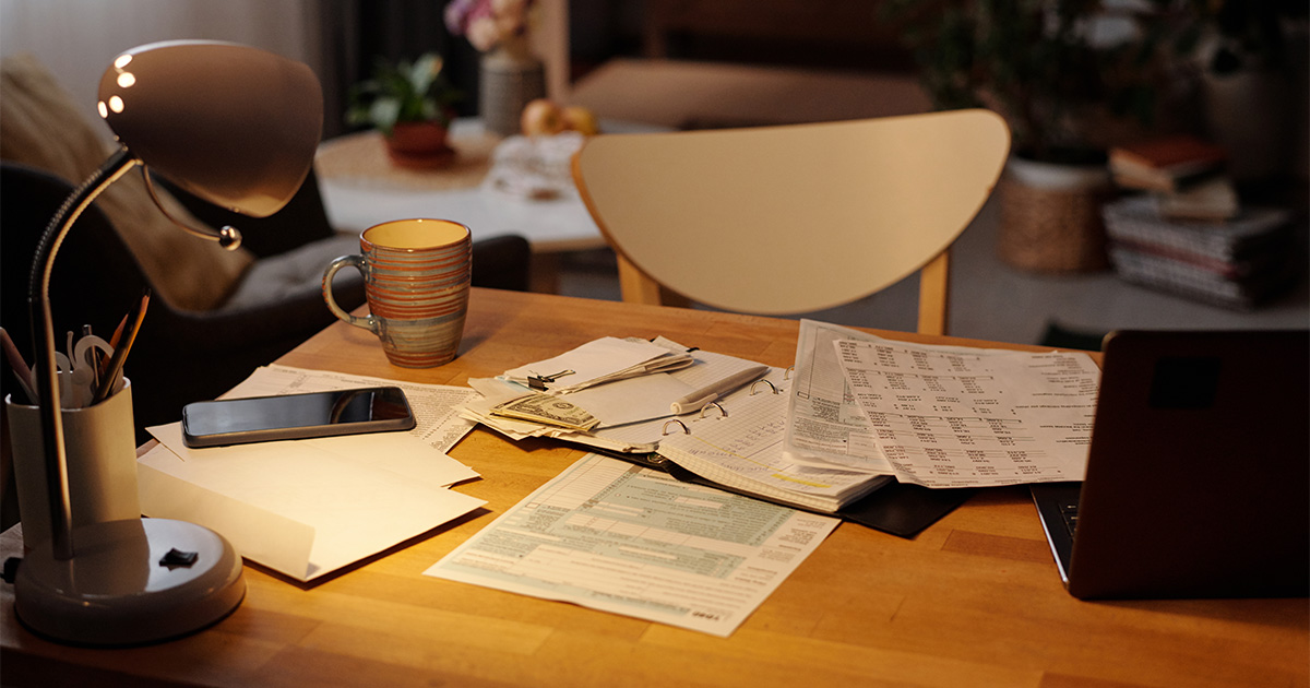 A table, smartphone and various papers and binders sit atop a kitchen table. There is a coffee cup next to these items. The person who lives in this home is trying to find the cheapest way to move cross country.