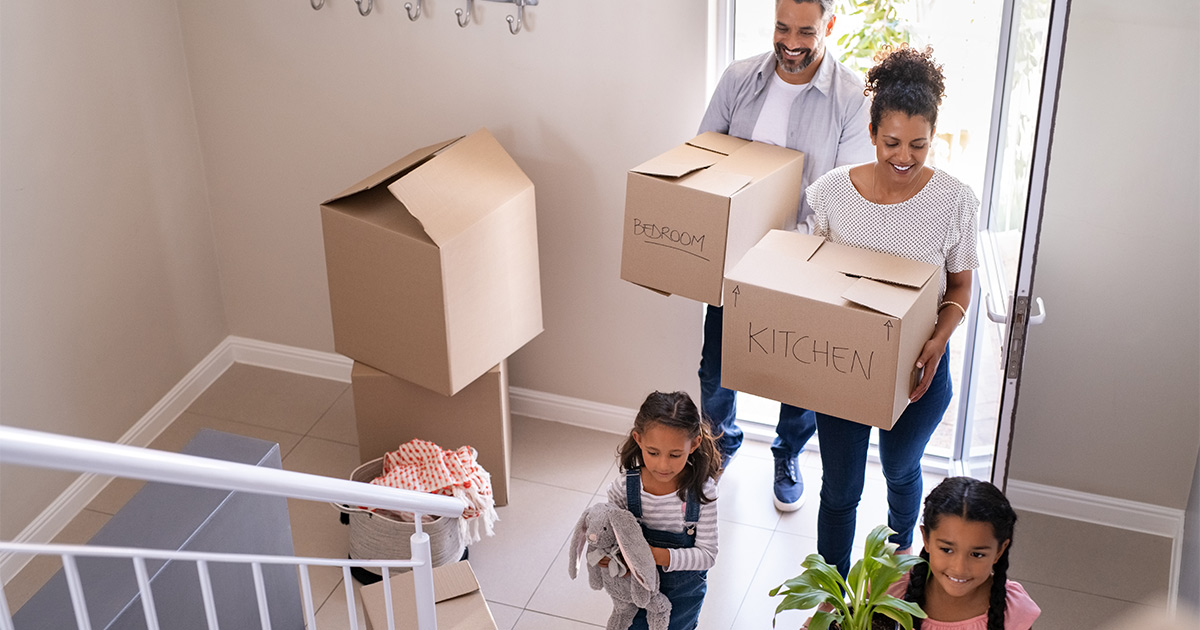 A family of four carry boxes into their new home. They used packing and unpacking services for their move.