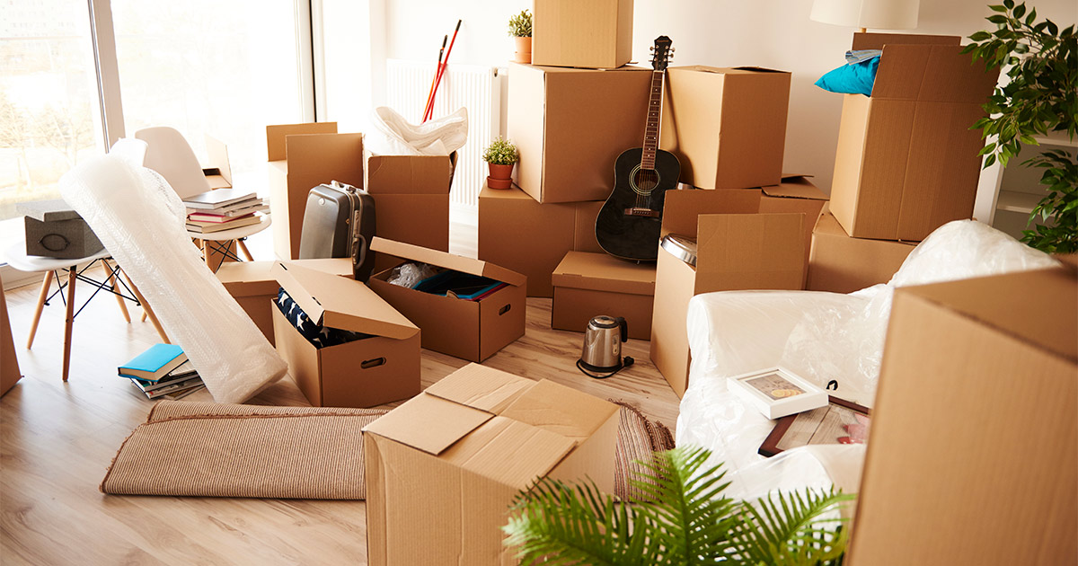 A large group of moving boxes are in a living room, with some items still needing to be packed surrounding them. These items are part of a small move and will be moved by full-service movers.