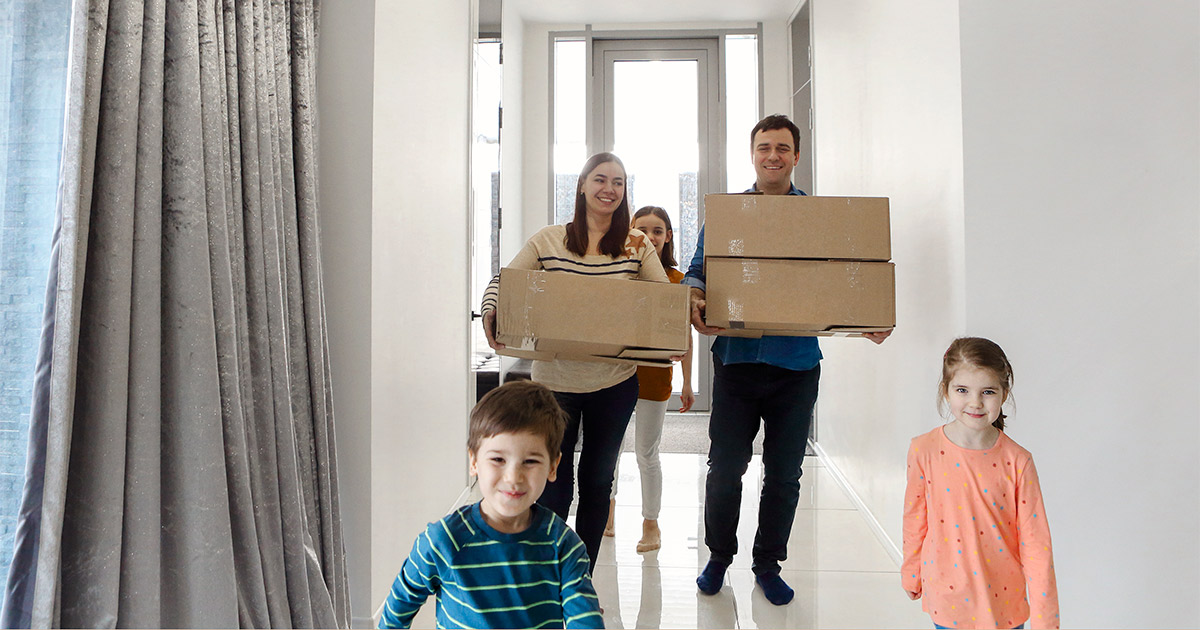 A family of four carries boxes into their new home. They have just moved, and it is the new year.