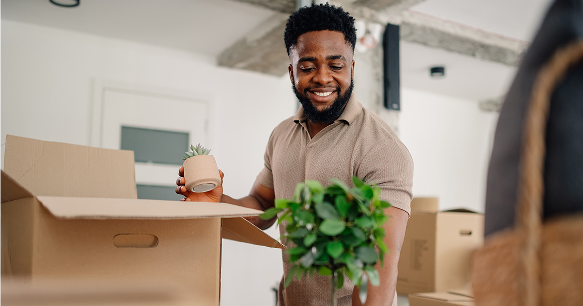 A man smiles while packing desk decorations. He just celebrated his last day of work and is going to start a new job soon.
