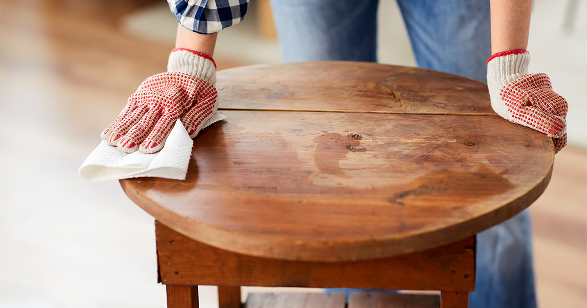 Someone wearing work gloves wipes down an antique table. It is being prepared to move cross country. 