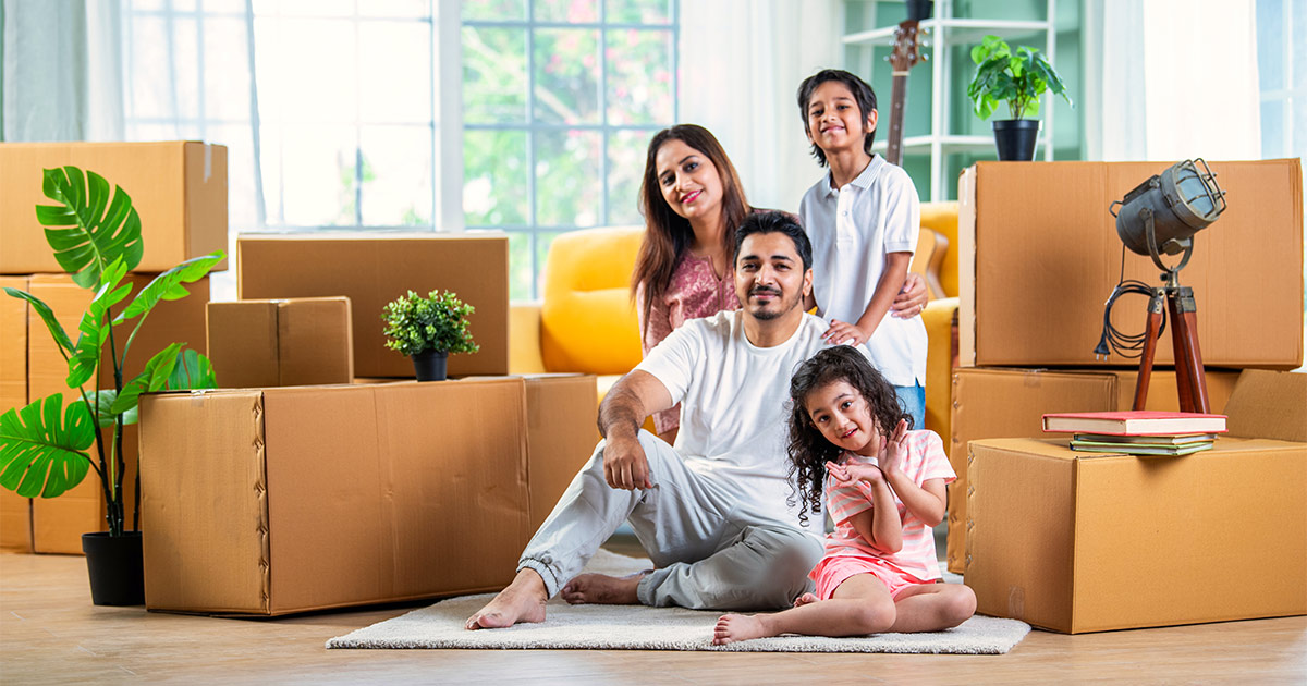 A family of four sits in their new living room surrounded by moving boxes. They have completed moving out of the country to their new home in the United Kingdom. They used an international moving company.
