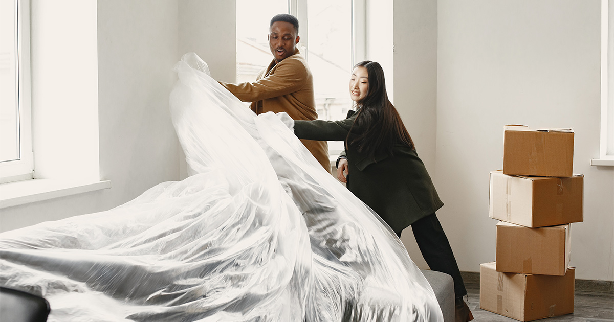 A couple takes the plastic wrap off their couch. Moving boxes are stacked nearby. They have just completed a move. Before they did, they compared long distance moving companies through a variety of factors beyond price.