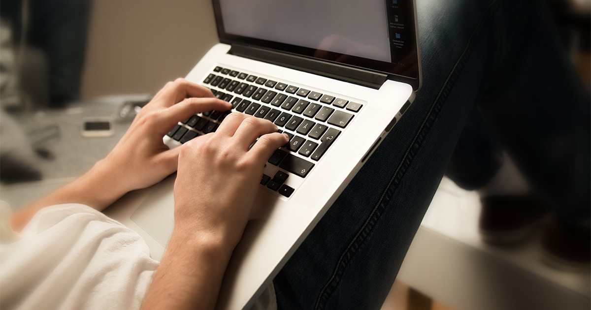 Someone sits on a couch with a laptop on their lap. They are using Reddit moving tips to research the best moving companies for their upcoming long distance move.