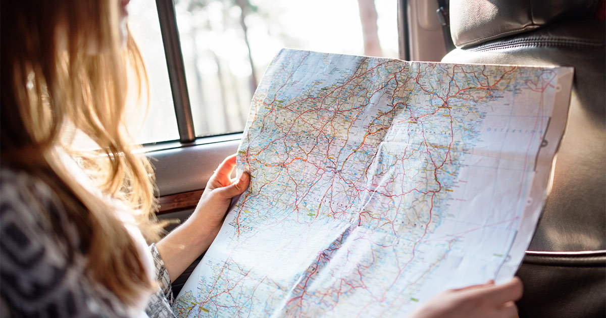 A woman sits in a car and looks at a map. She is moving cross country and is excited to see what kinds of landmarks she will see along the way she she completes this move. 